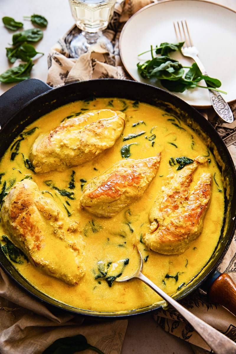 top down view of chicken breasts in cream sauce with spinach in black pan