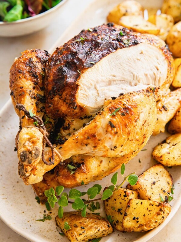 whole chicken on platter with roast potatoes around it