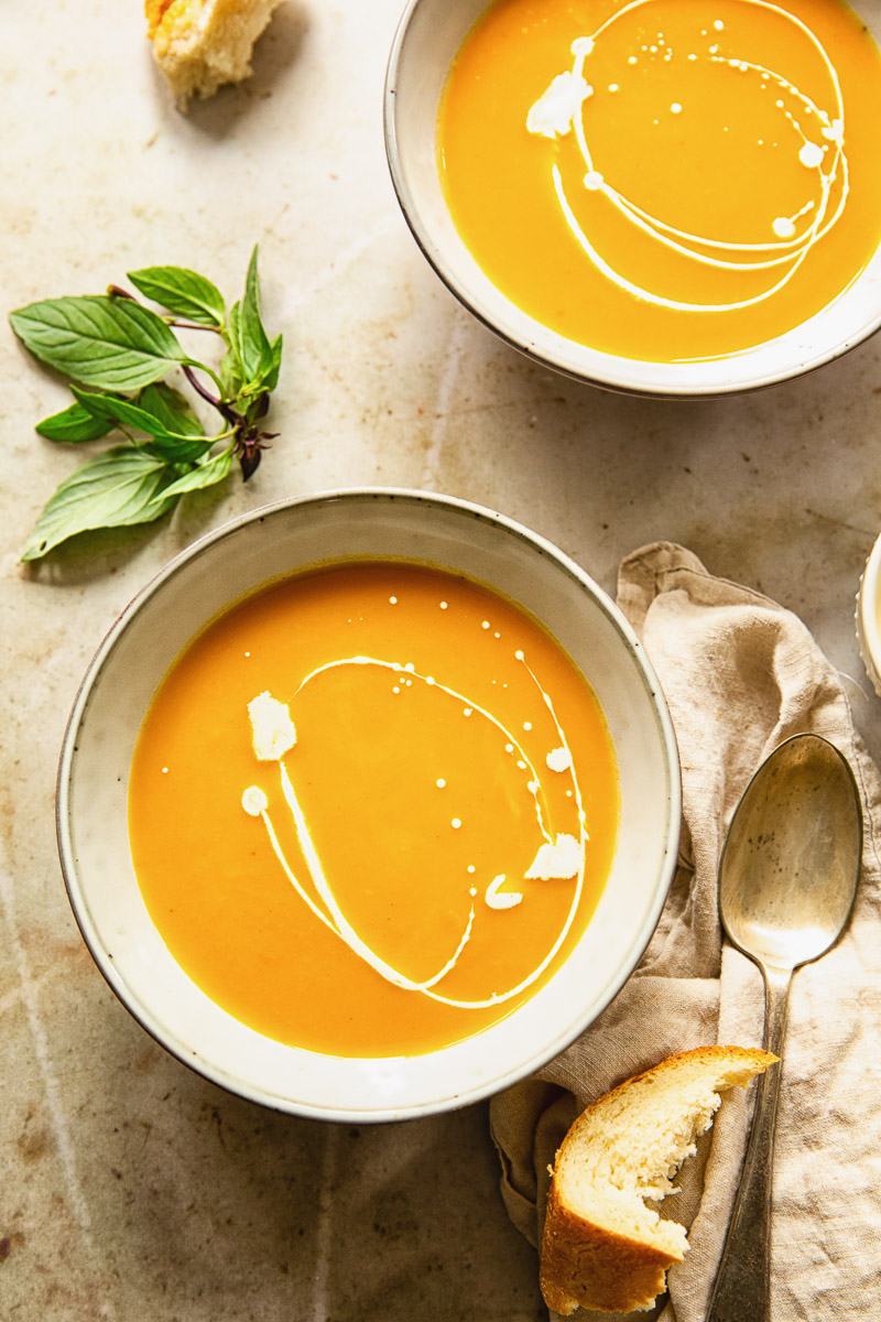 top down view of two bowls of squash and sweet potato soup and Thai basil leaves