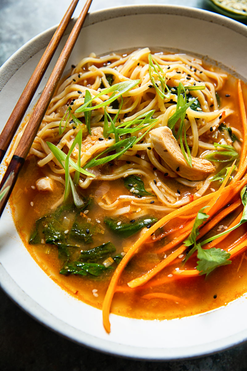 close up image of noodles in broth with chicken, carrots and green onions