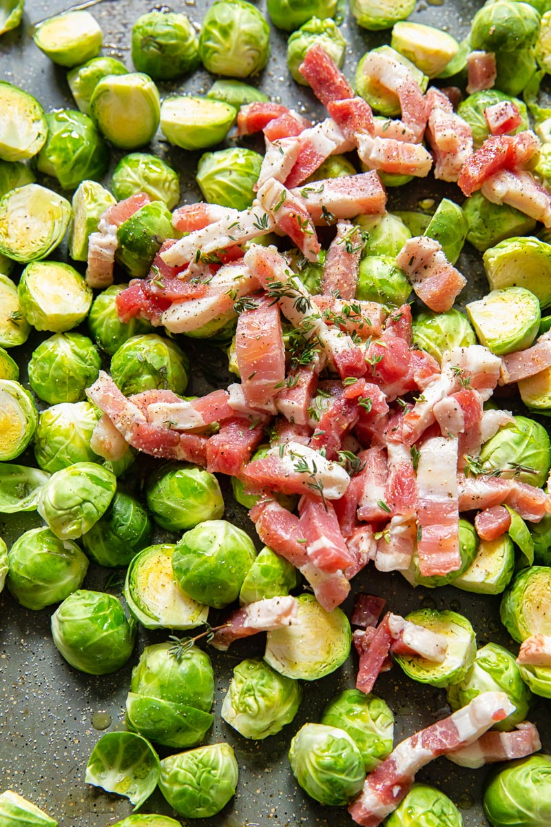 raw brussels sprouts topped with sliced bacon in roasting pan
