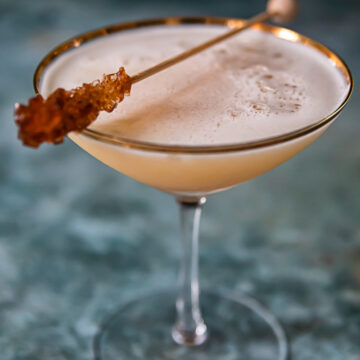 whisky sour in cocktail glass with brown sugar stir stick resting on top