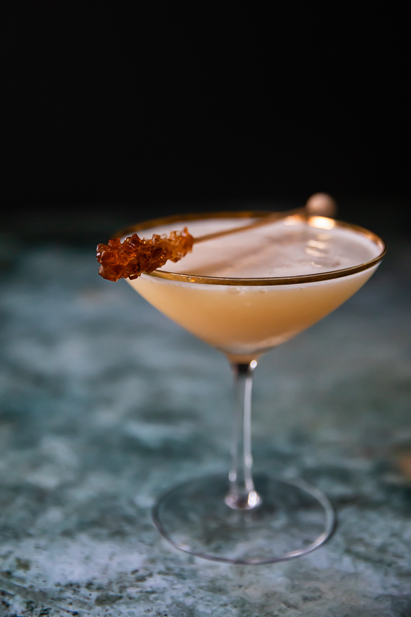 whisky sour in cocktail glass with brown sugar stir stick resting on top