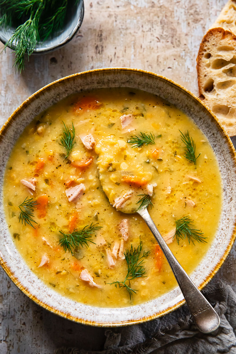 top down view of yellow split pea soup with ham and sprinkled with dil, a slice of bread near the bowl