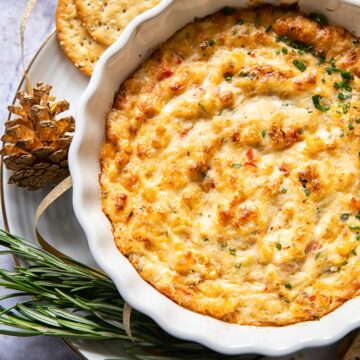 baked crab dip in white round dish with crackers and rosemary around the dish