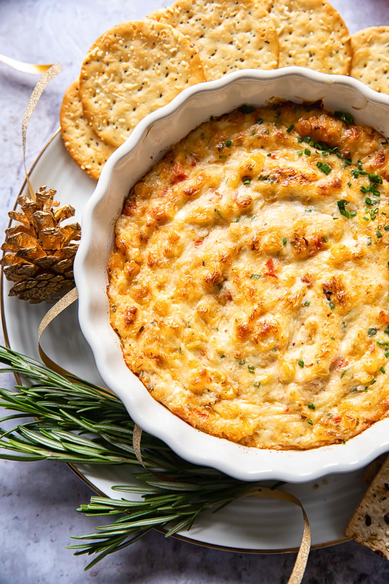 baked crab dip in white round dish with crackers and rosemary around the dish