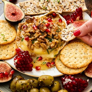baked brie topped with walnuts and pomegranate seeds, crackers, figs and olives around the plate.
