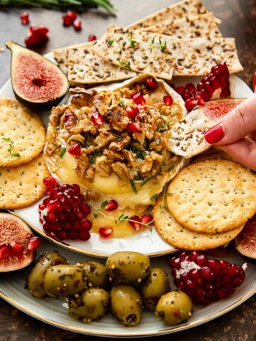 baked brie topped with walnuts and pomegranate seeds, crackers, figs and olives around the plate.