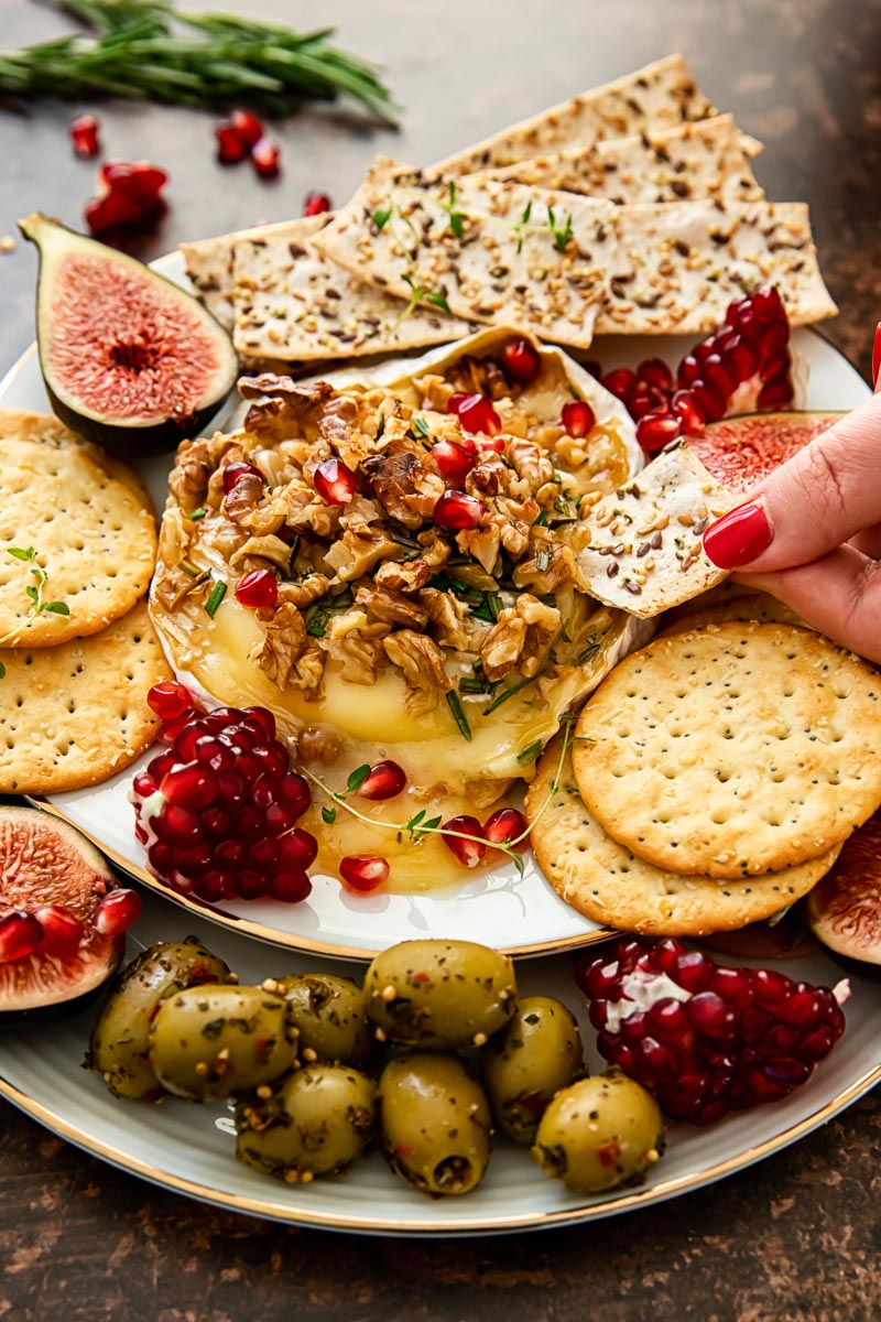 baked brie topped with walnuts and pomegranate seeds, crackers, figs and olives around the plate.