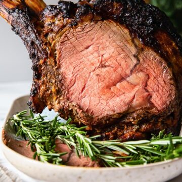 prime rib on a platter with fresh rosemary in the foreground