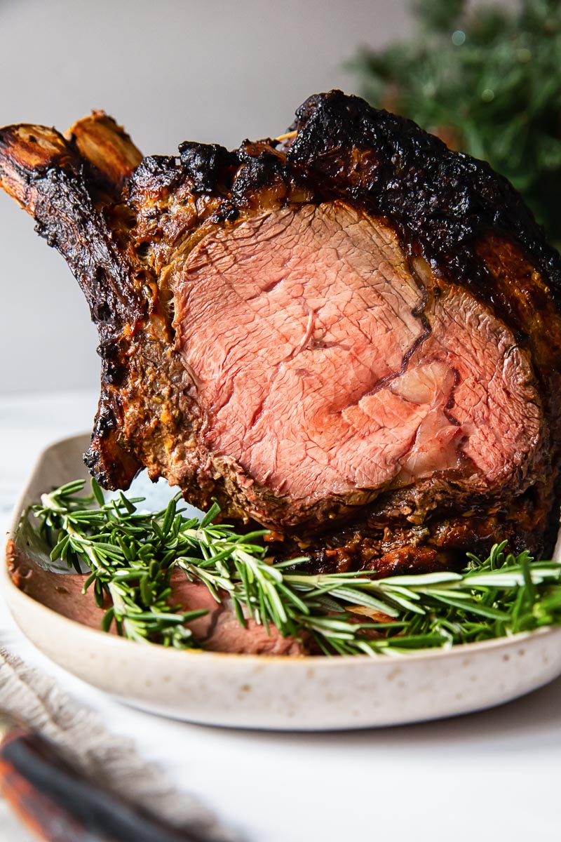 prime rib on a platter with fresh rosemary in the foreground