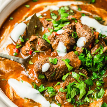 beef goulash with sour cream and parsley in cream coloured pot