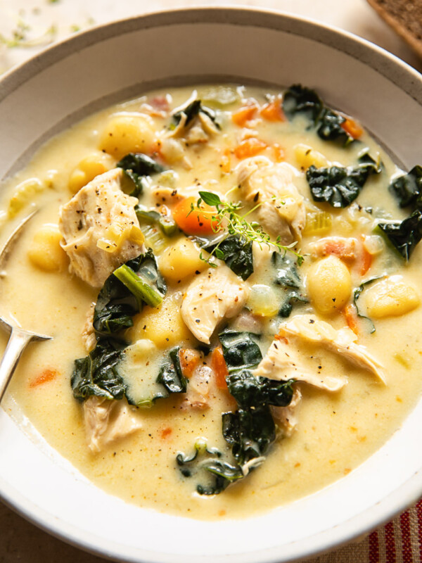 chicken gnocchi soup in a cream coloured bowl with a spoon in it