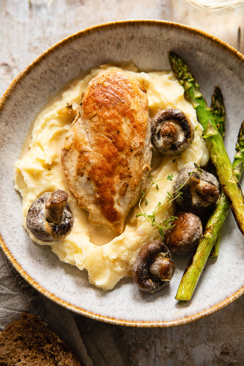 chicken breast and mushrooms on top of mashed potatoes and asparagus on the side