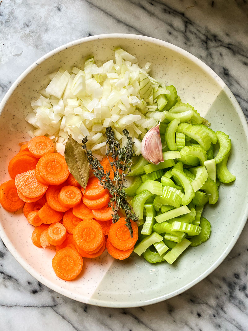 mirepoix in a bowl (diced carrots, onions and celery) with bay leaf, thyme and garlic clove