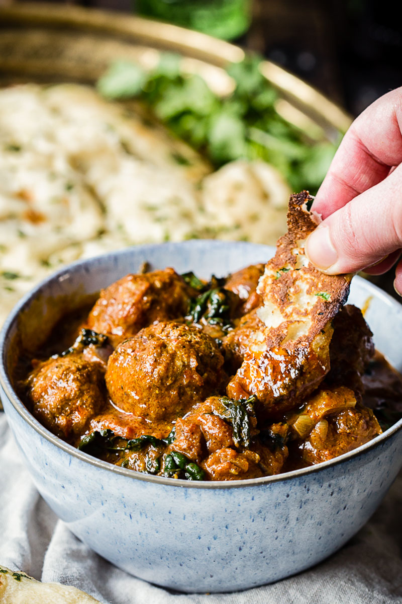 meatballs in a blue bowl and a hand dipping flatbread into the curry sauce