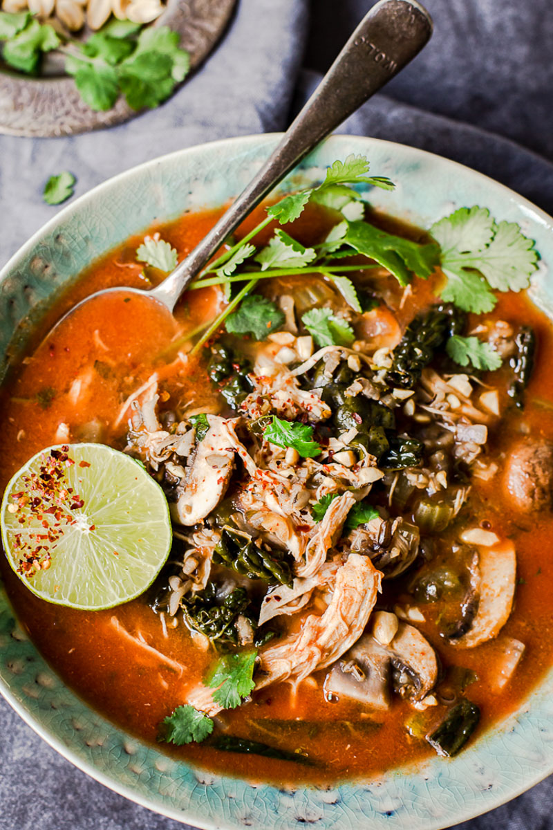 top down view of Thai chicken and rice soup topped with sliced line and cilantro in a blue bowl.