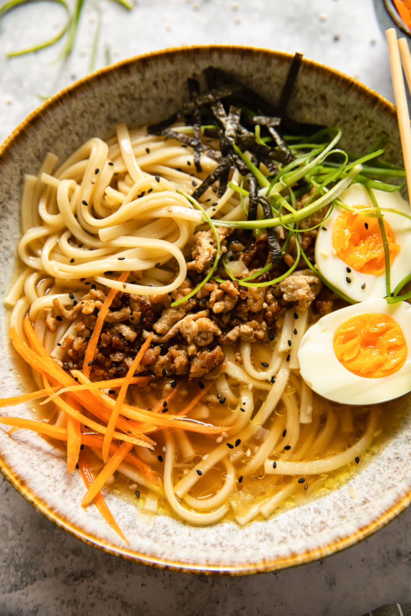 noodle soup topped with boiled egg, matchstick carrots and green onions