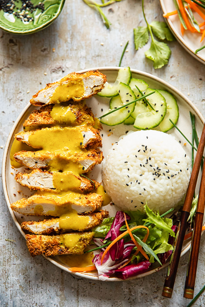 top down view of a plate with chicken Katsu curry, rice, sliced cucumber and salad