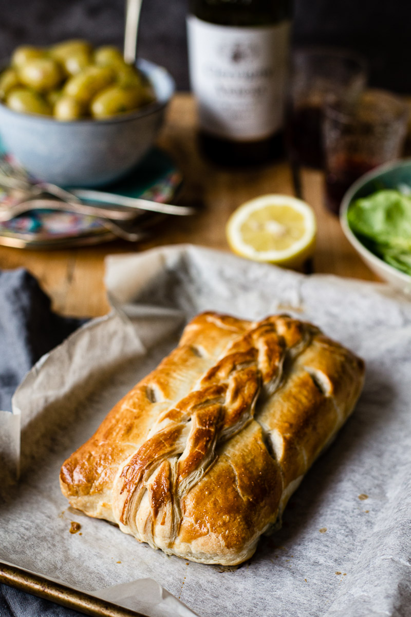 Salmon en croute on baking sheet with a bowl of baby potatoes in the background and a bottle of wine