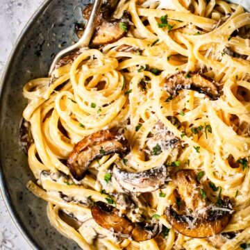 tagliatelle with mushrooms and bacon in a blue bowl with two forks in