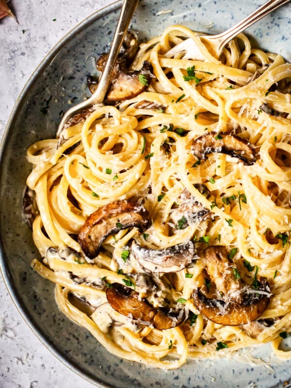 tagliatelle with mushrooms and bacon in a blue bowl with two forks in