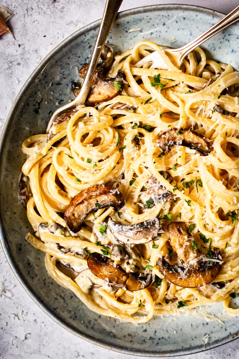 tagliatelle with mushrooms and bacon in a blue bowl with two forks in