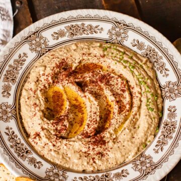 baba ganoush in a bowl sprinkled with sumac and chives on brown background.