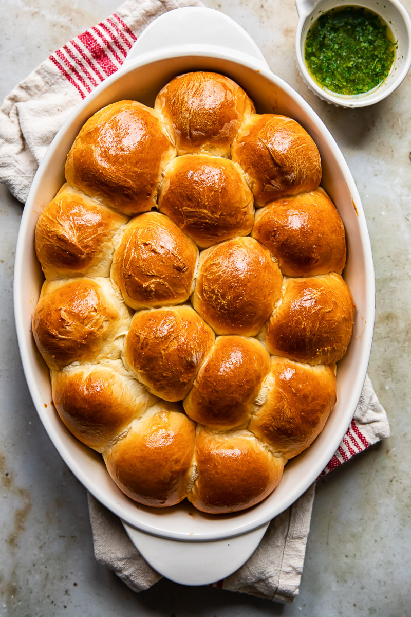 top down view of dinner rolls in oven pan, melted garlic butter in a small bowl next to it.