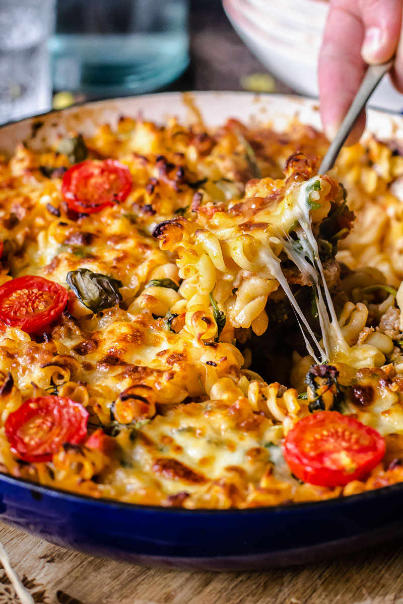 side view of sausage pasta casserole with a hand holding a spoon