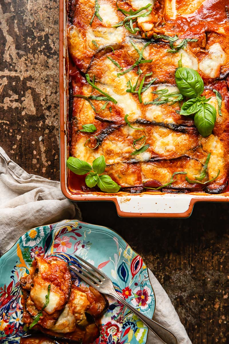 top down view of aubergine parmigiana in a pan and a portion on a blue plate