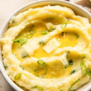 mashed potatoes topped with melted butter and sliced green onions in a bowl