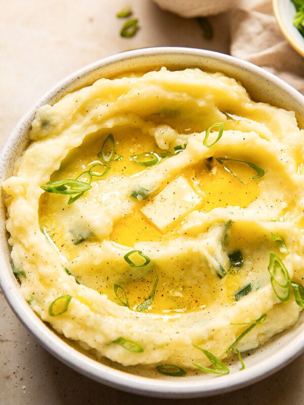 mashed potatoes topped with melted butter and sliced green onions in a bowl