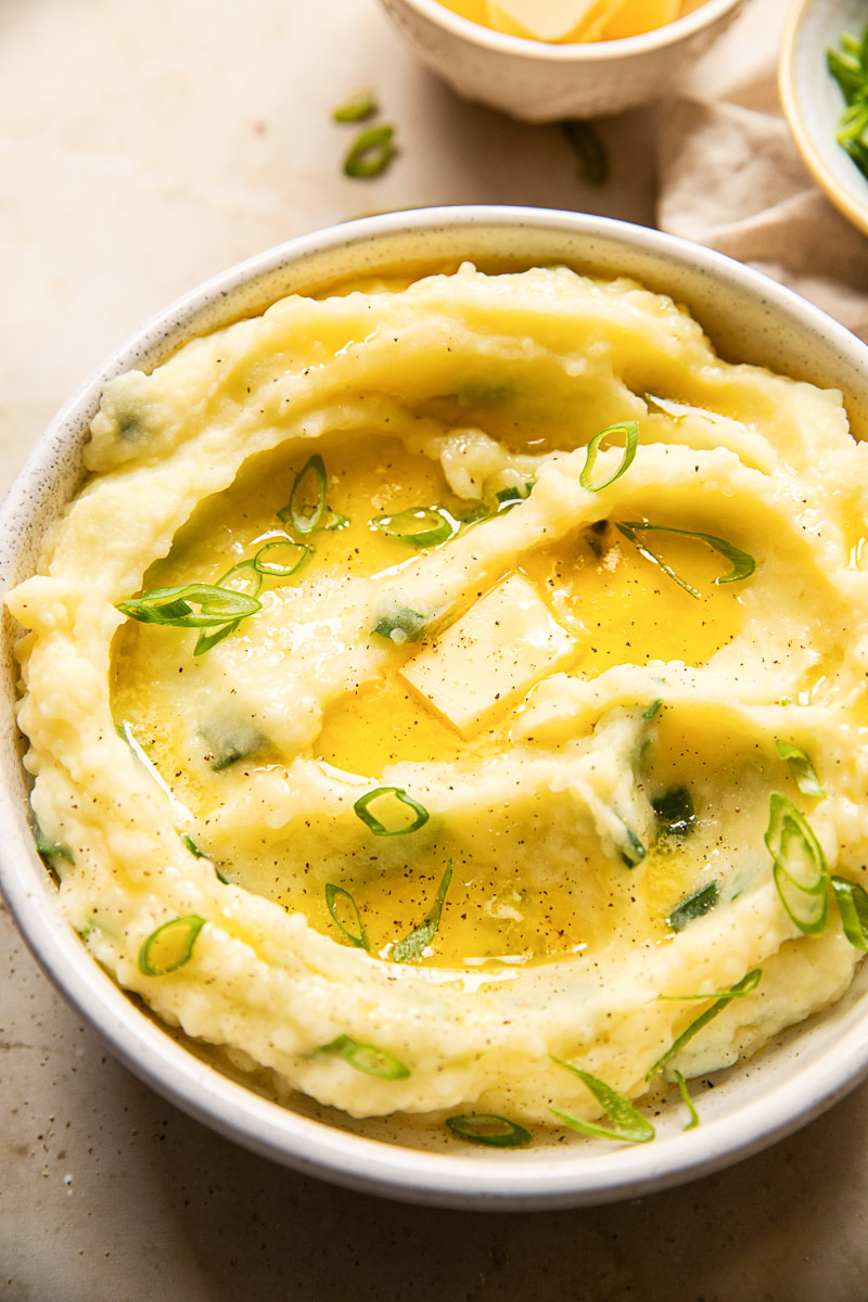 mashed potatoes topped with melted butter and sliced green onions in a bowl