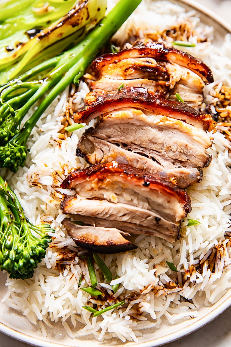 pork sliced on top of rice, broccoli on a plate