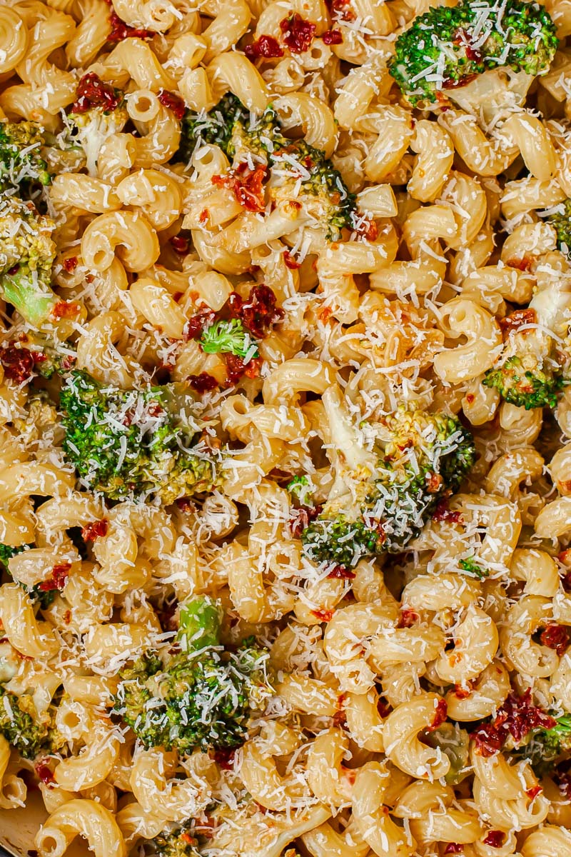 top down view of pasta dish with broccoli and sun-dried tomatoes sprinkled with Parmesan cheese