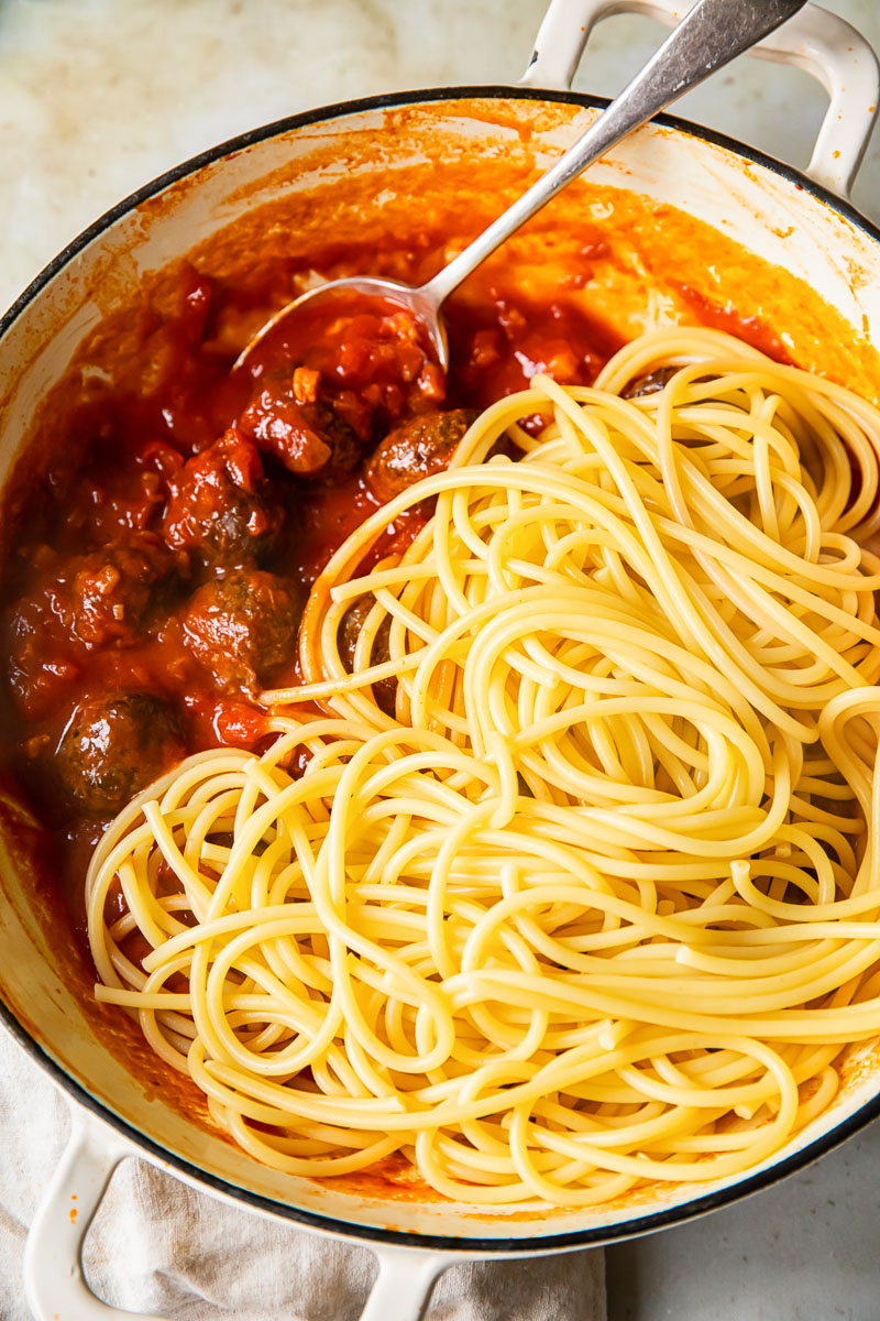 top down view of bucatini on top of red sauce with meatballs in a pan.