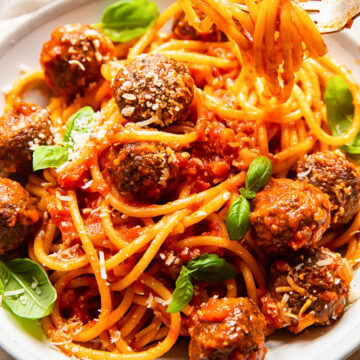 bucatini with meatballs in a cream coloured bowl, topped with fresh basil leaves