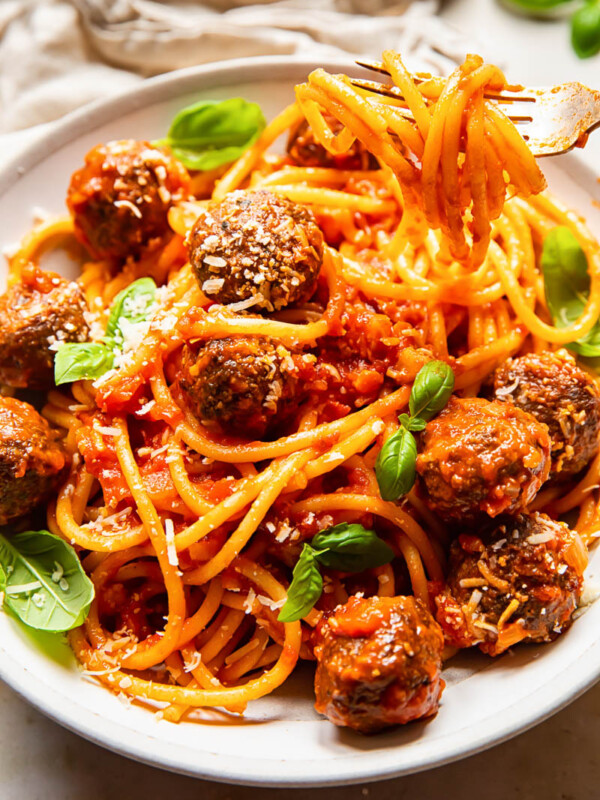 bucatini with meatballs in a cream coloured bowl, topped with fresh basil leaves