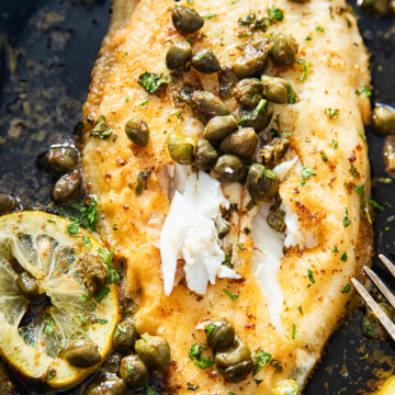 close us of sole topped with capers and lemon sliced in cast iron pan