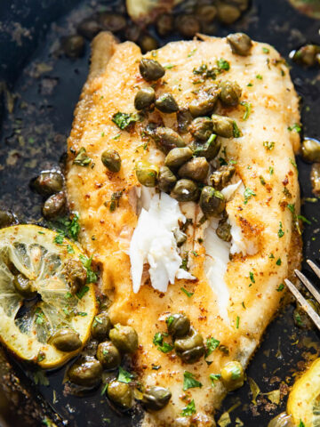 close us of sole topped with capers and lemon sliced in cast iron pan