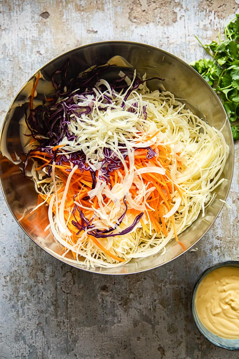 homemade slaw mix in a stainless steel bow, mayonnaise dressing next to it in a small blue bowl.