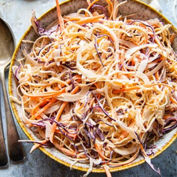 top down view of coleslaw in a bowl, a spoon and napkin.