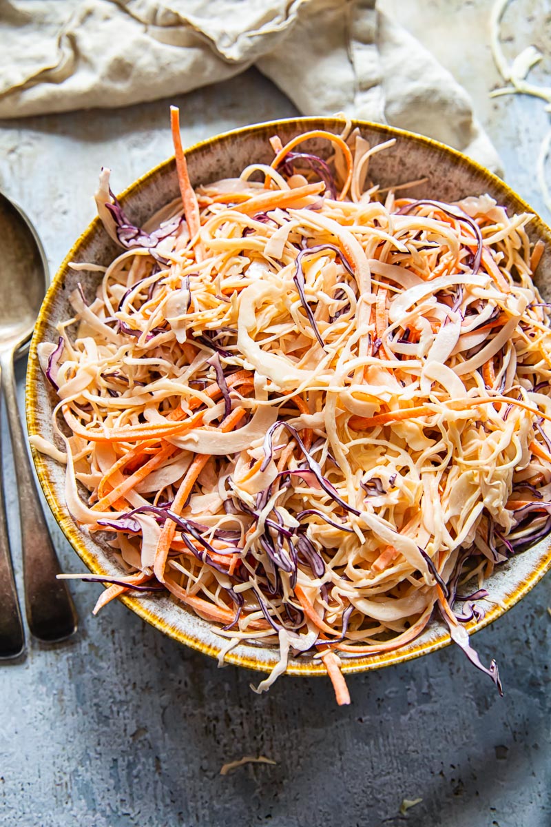 top down view of coleslaw in a bowl, a spoon and napkin.