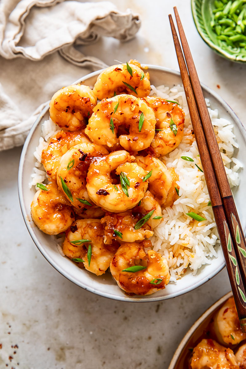 top down view of shrimp on top of rice in a bowl with chopsticks, sliced green onions and a napkin.