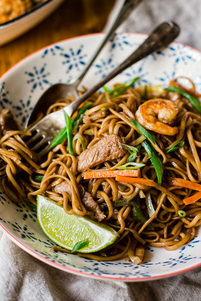 Filipino Noodles in a bowl with a fork and spoon and a lime wedge