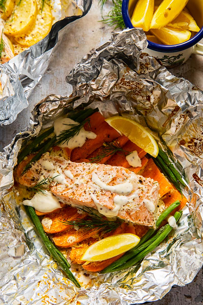 salmon on top of sweet potatoes and green beans in a foil packet.