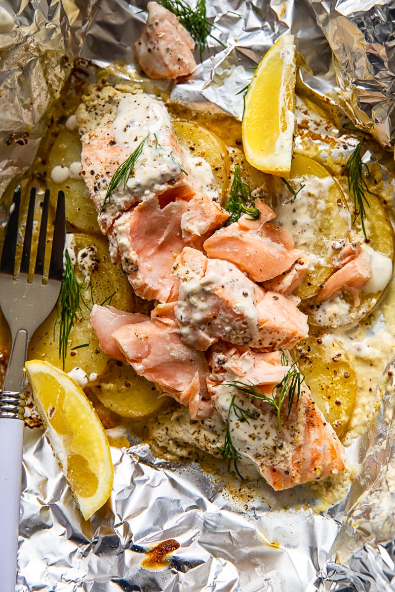 flaked fish on top of potato slices in foil, lemon wedges.