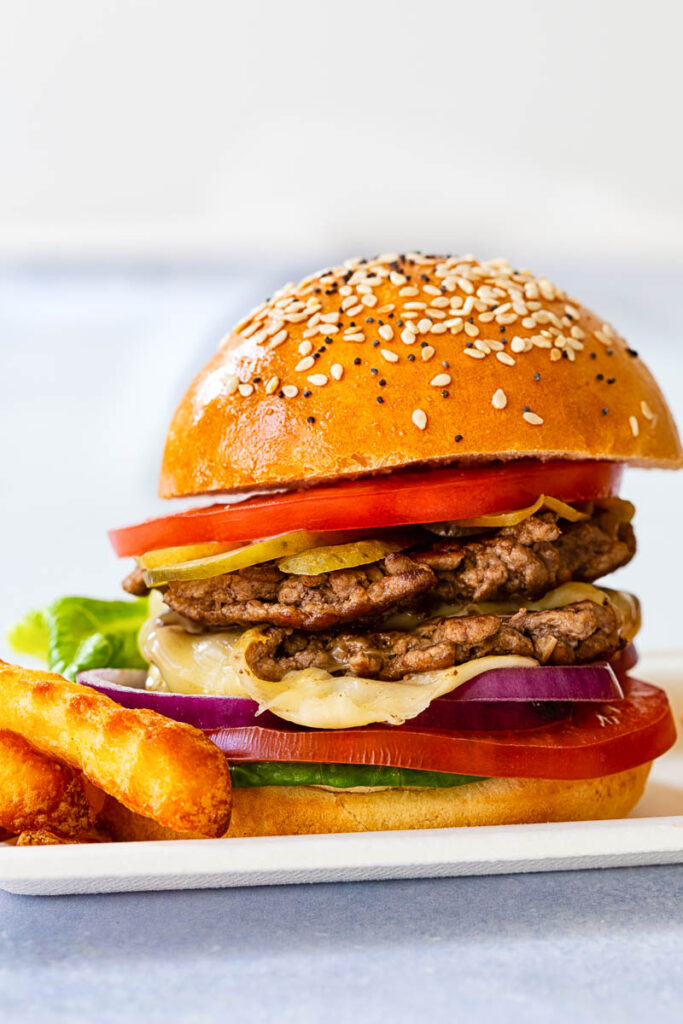 side view smash burger with sliced tomatoes, pickles and lettuce