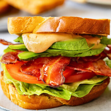 close up of BLT sandwich with avocado and sauce spilling over